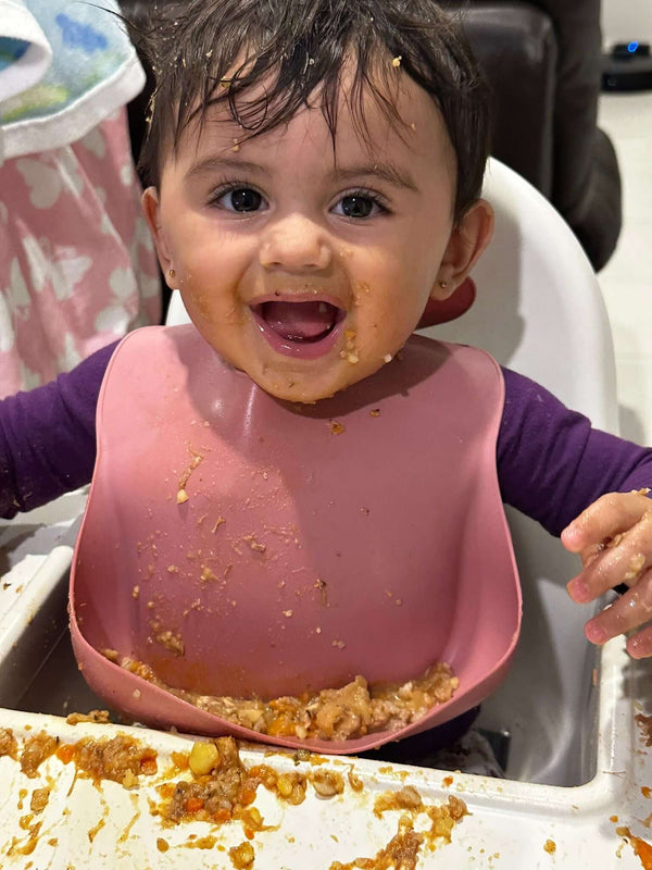 Happy baby enjoying mealtime with messy face and highchair, showcasing joy of trying new textures.