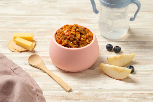 Bowl of slow cooked beef and barley puree with vegetables beside pear and blueberries, perfect for babies.