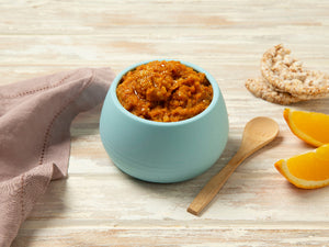 Blue bowl with orange spread on a wooden surface with a napkin and oranges.