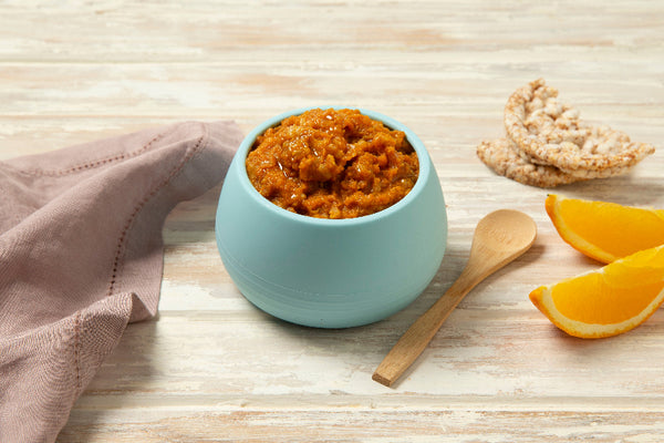 Blue bowl with orange spread on a wooden surface with a napkin and oranges.