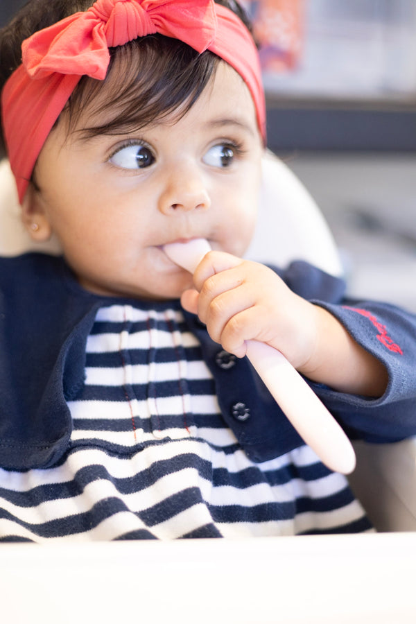 Child with a red headband and striped outfit holding a Tiny Turtle Spoon