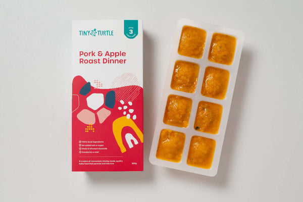 Pork and Apple Roast Dinner Stage 3 baby food by Tiny Turtle, featuring lumpy textured puree in tray next to packaging.