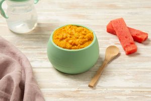 Bowl of stage 3 summer mango chicken with brown rice baby food with lumpy puree with watermelon pieces on a wooden surface.